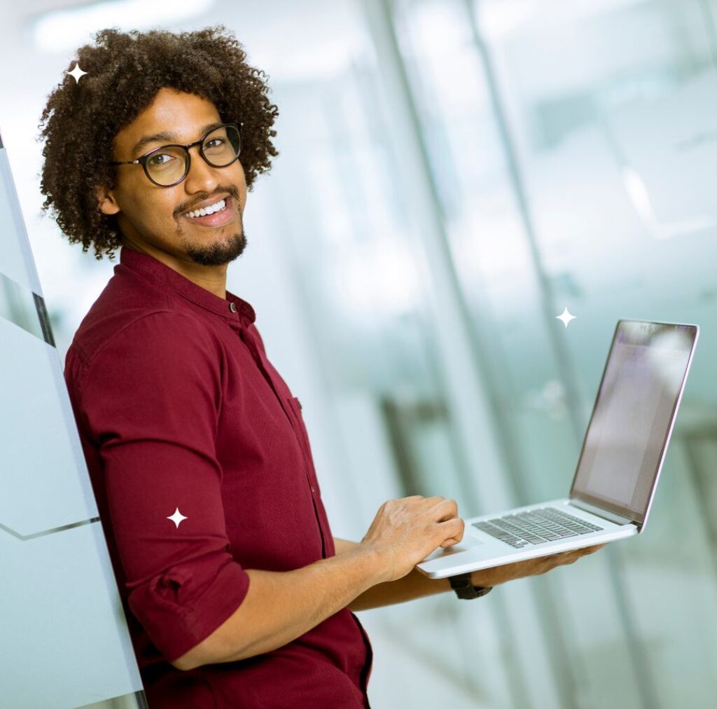 Black man pressing laptop leaning against the wall in a digital marketing agency office.